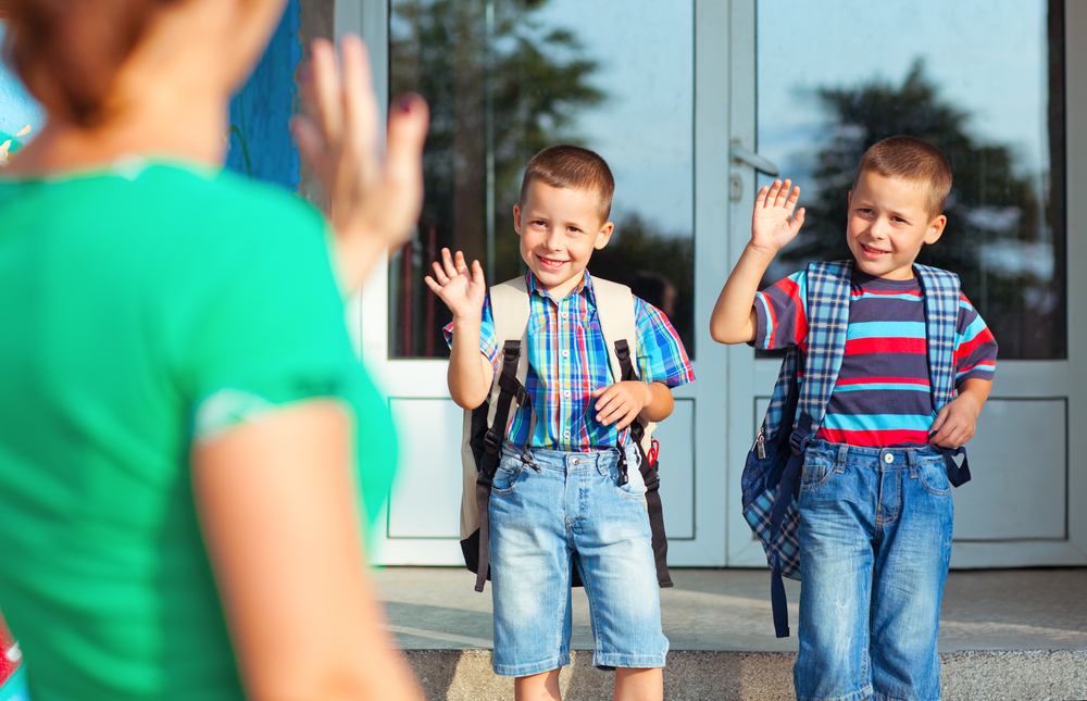 Two brothers waving back at their mother on their first day at school.